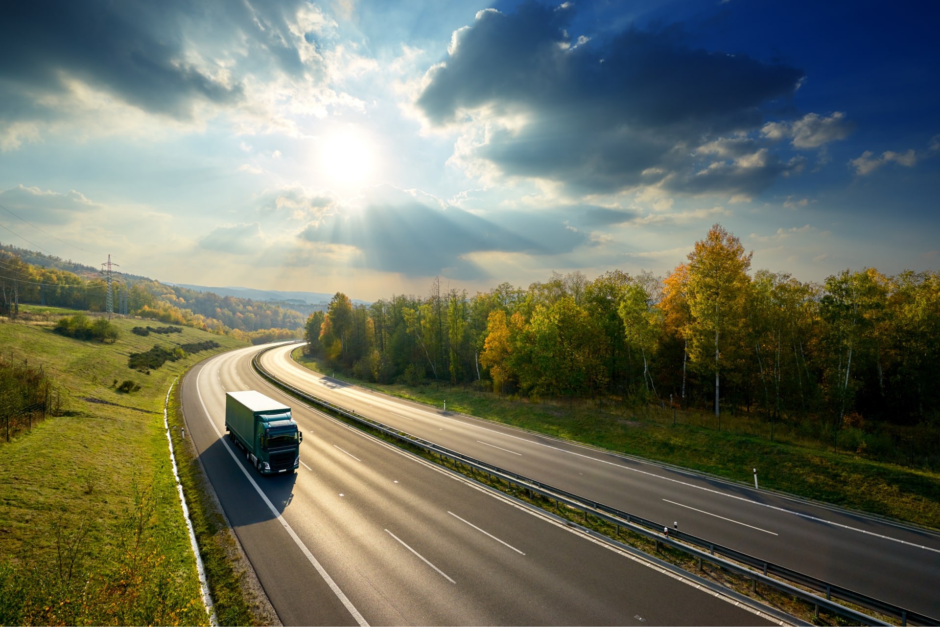 Refrigerated truck driving on a sunlit highway lined with autumn trees