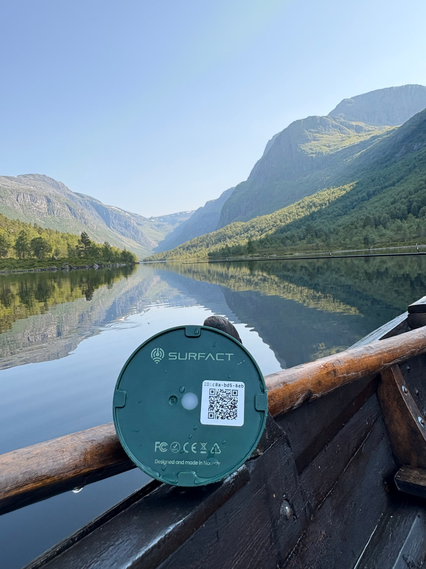 Emma Smart Tracker resting on the oar of a wooden rowing boat on a still Norwegian fjord, engraved Designed and made in Norway