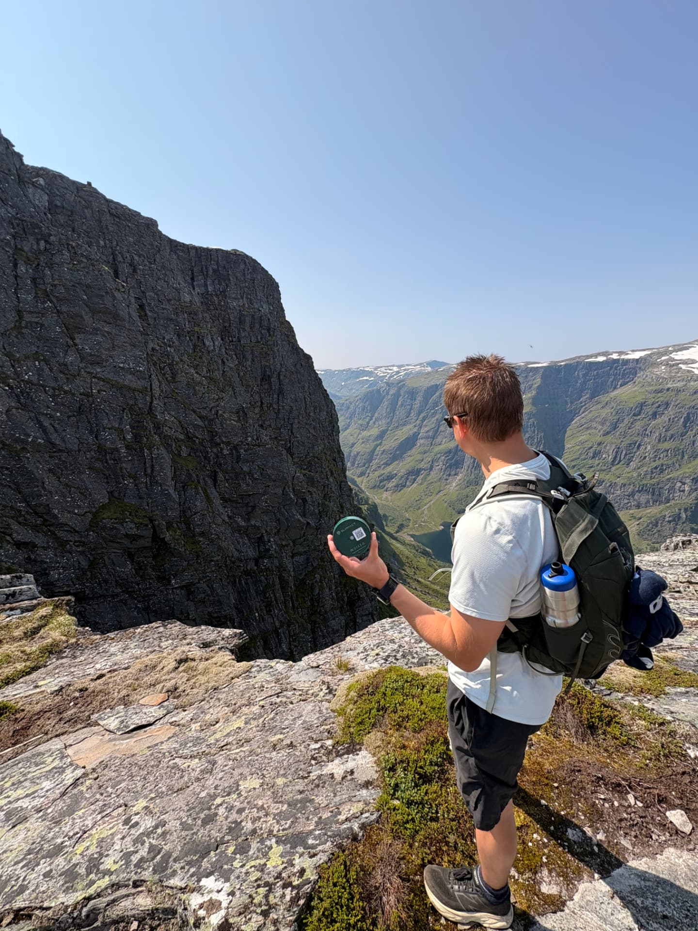 Surfact team member holding an Emma Smart Tracker on a mountain edge above a Norwegian valley